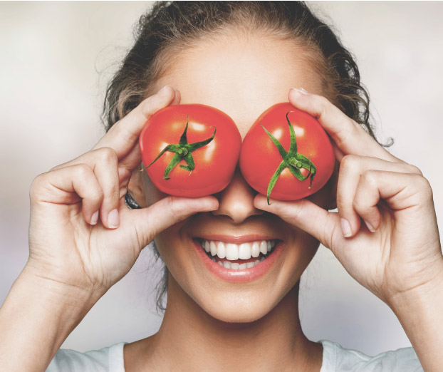 Frau hält sich lachend Tomaten vor die Augen